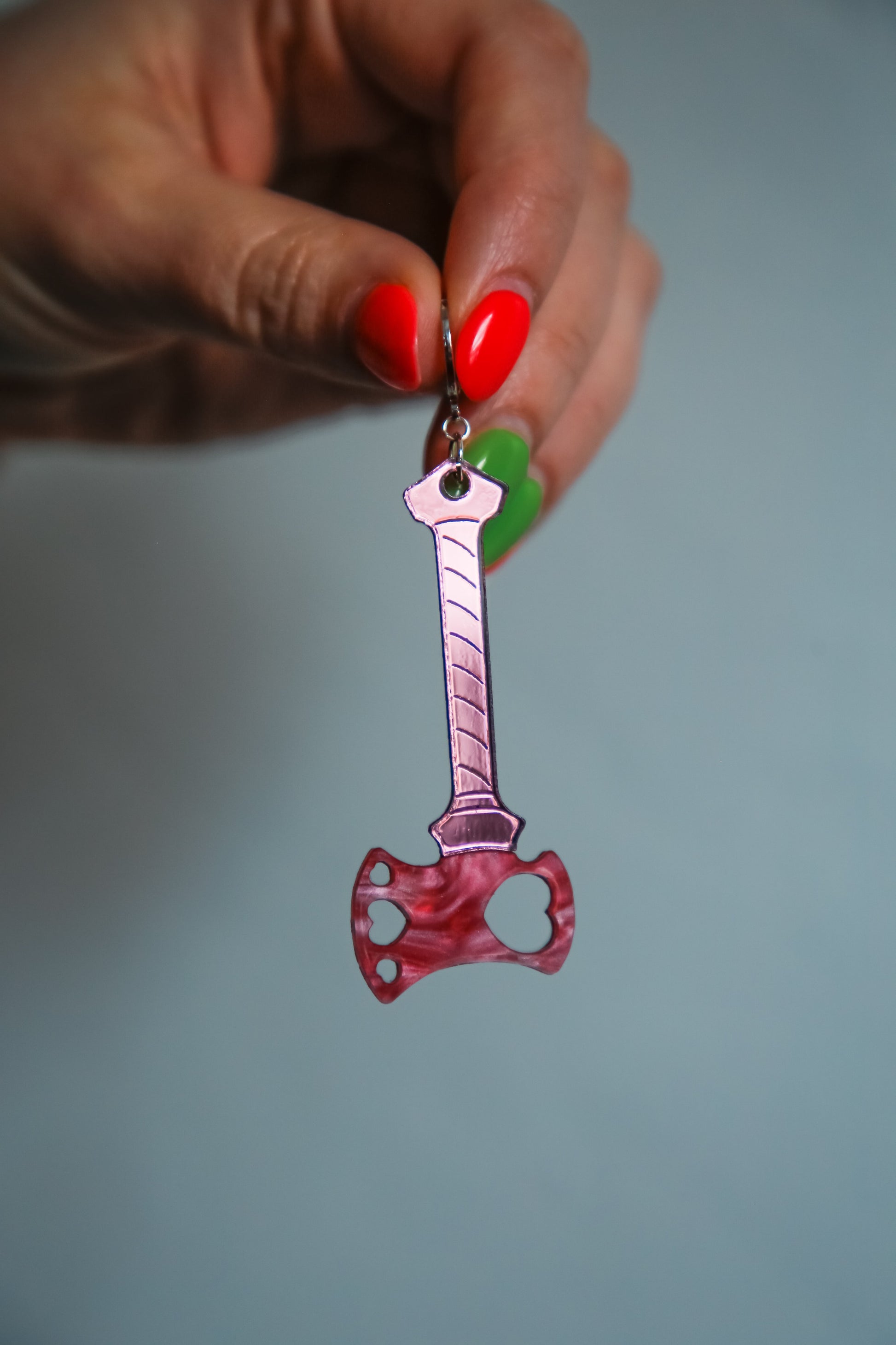 axe acrylic earring with pink blade and reflective pink handle being held by a hand