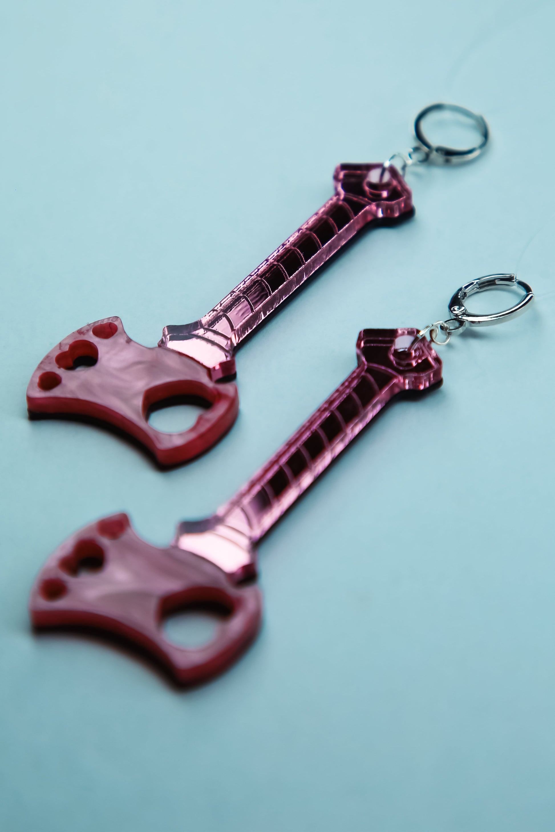 axe acrylic earrings with pink blade and reflective pink handle against a blue background