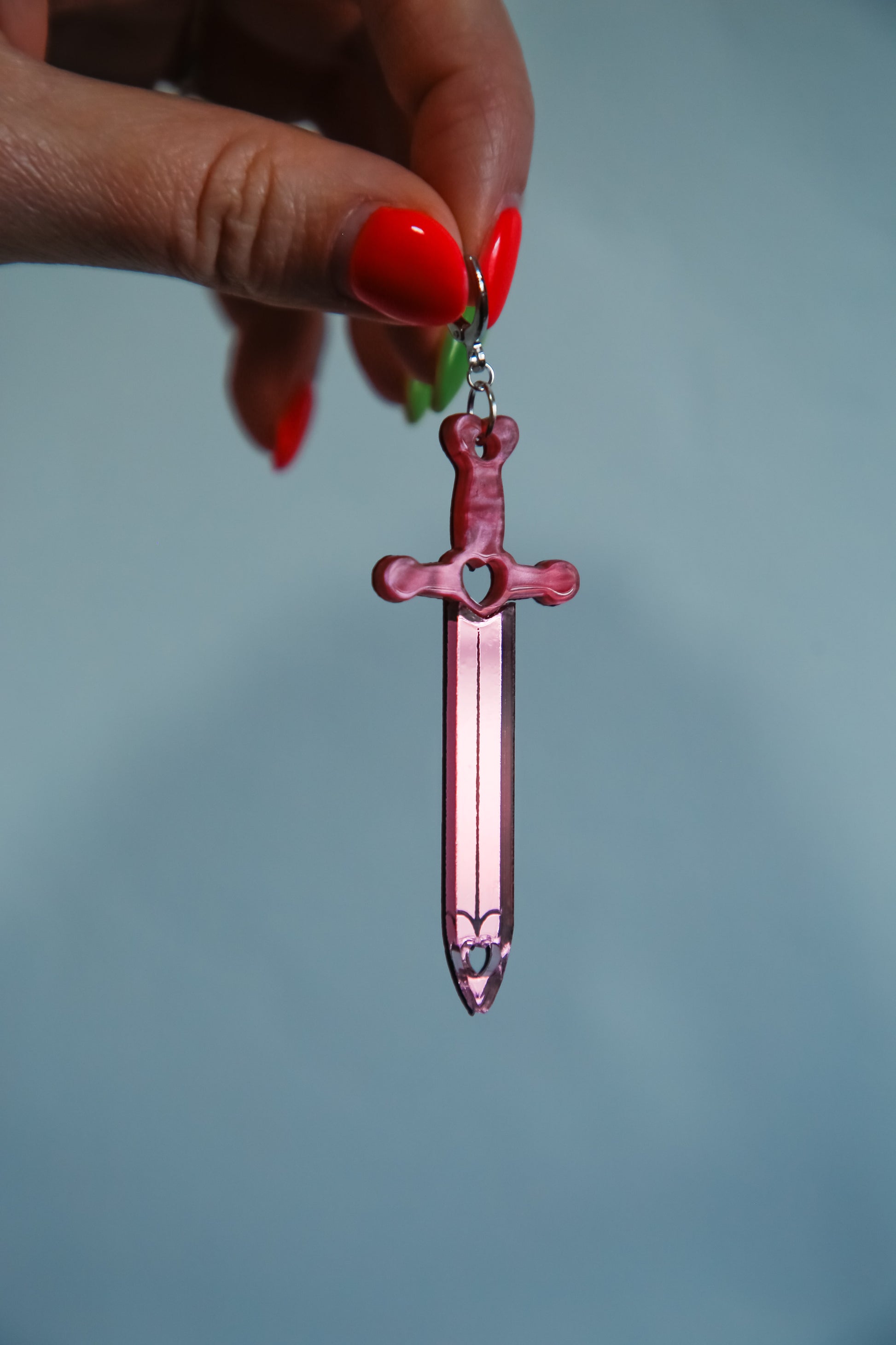 Pink sword acrylic earring with a reflective pink blade being held by a hand