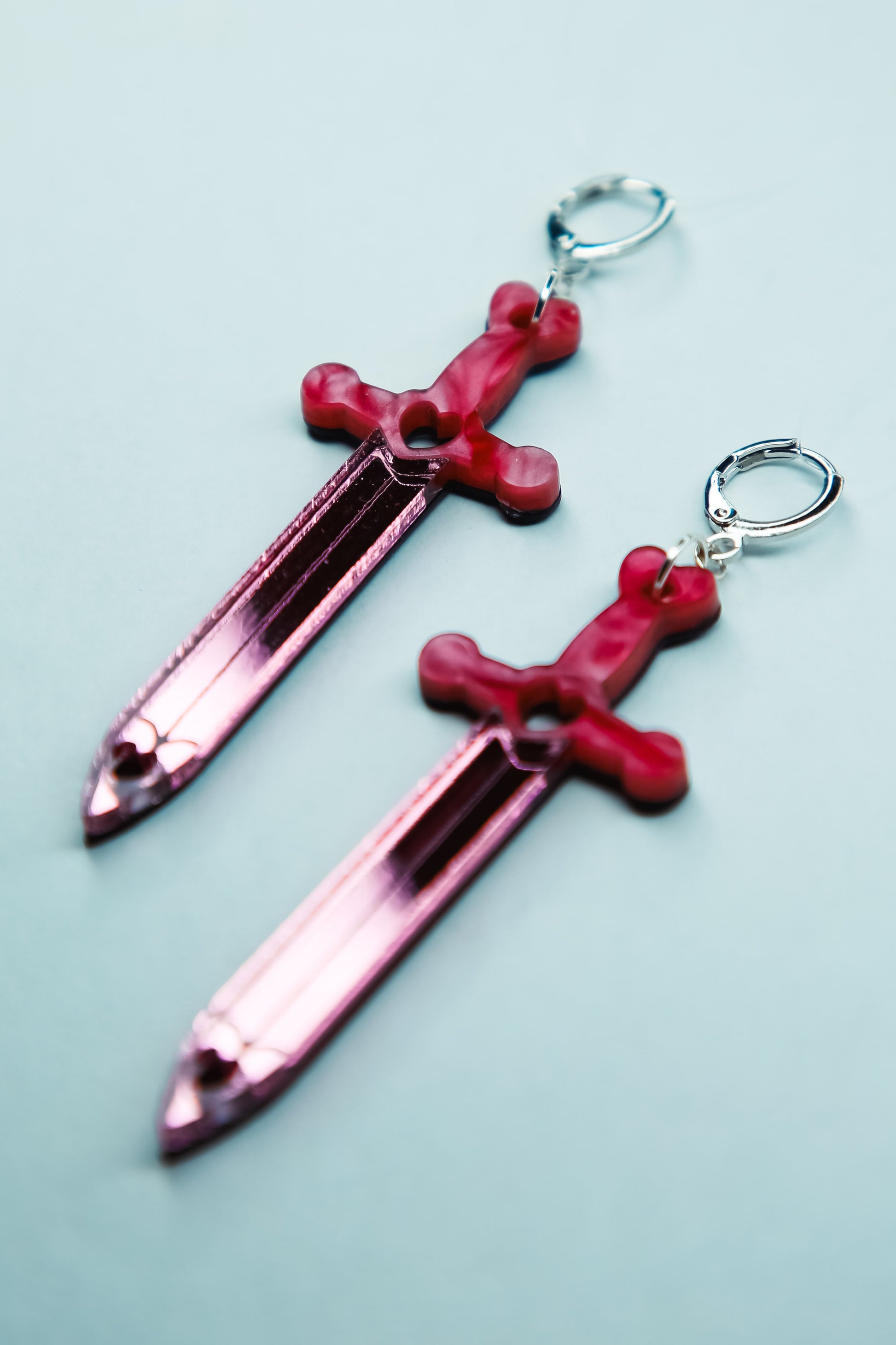 a pair of pink sword acrylic earrings with a reflective pink blade