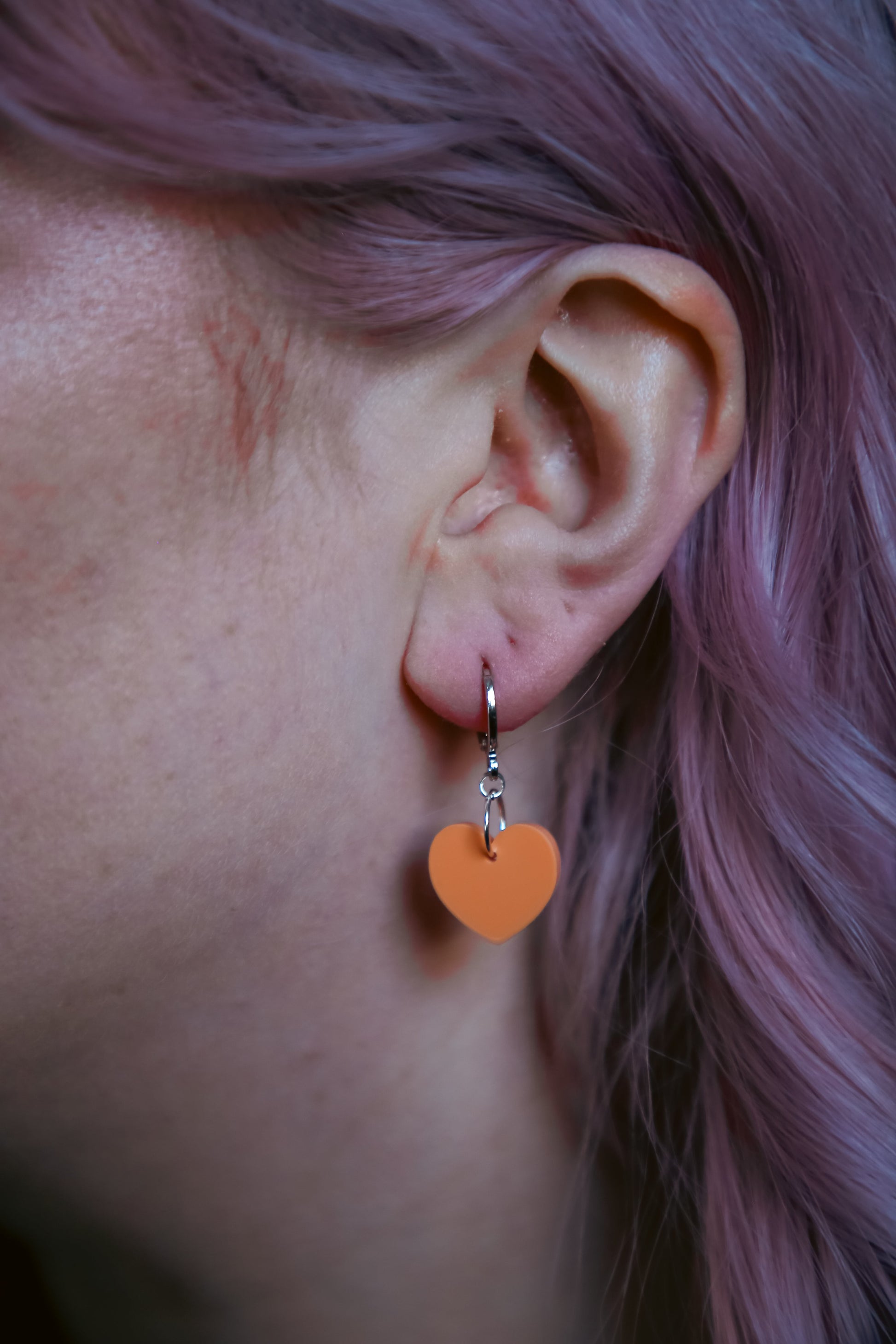 A pastel orange heart acrylic earring on an ear