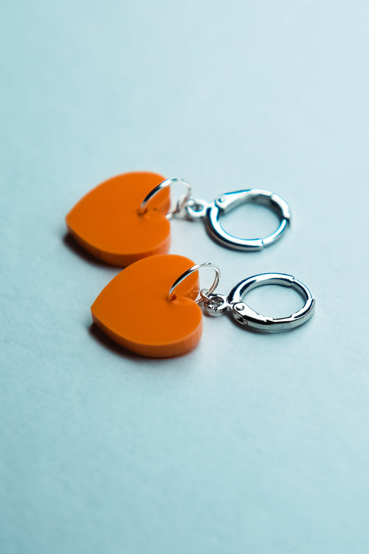A pastel orange heart acrylic earring on a blue background
