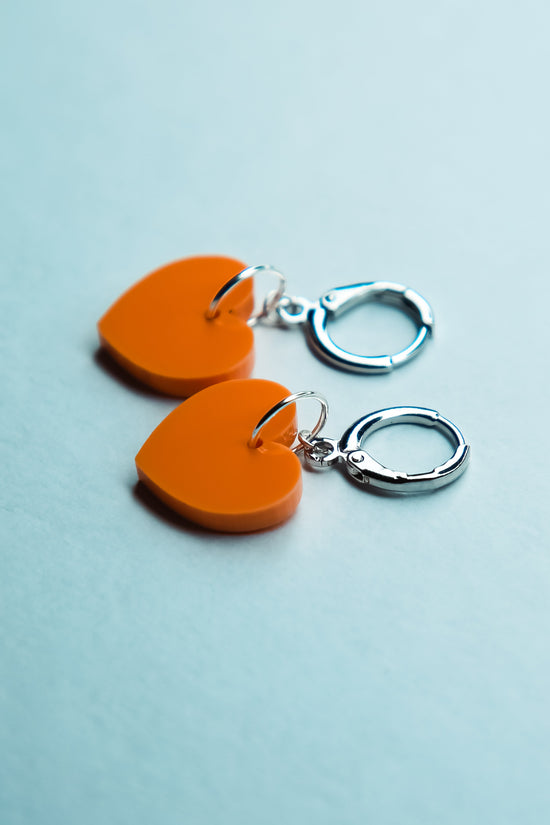 A pastel orange heart acrylic earring on a blue background