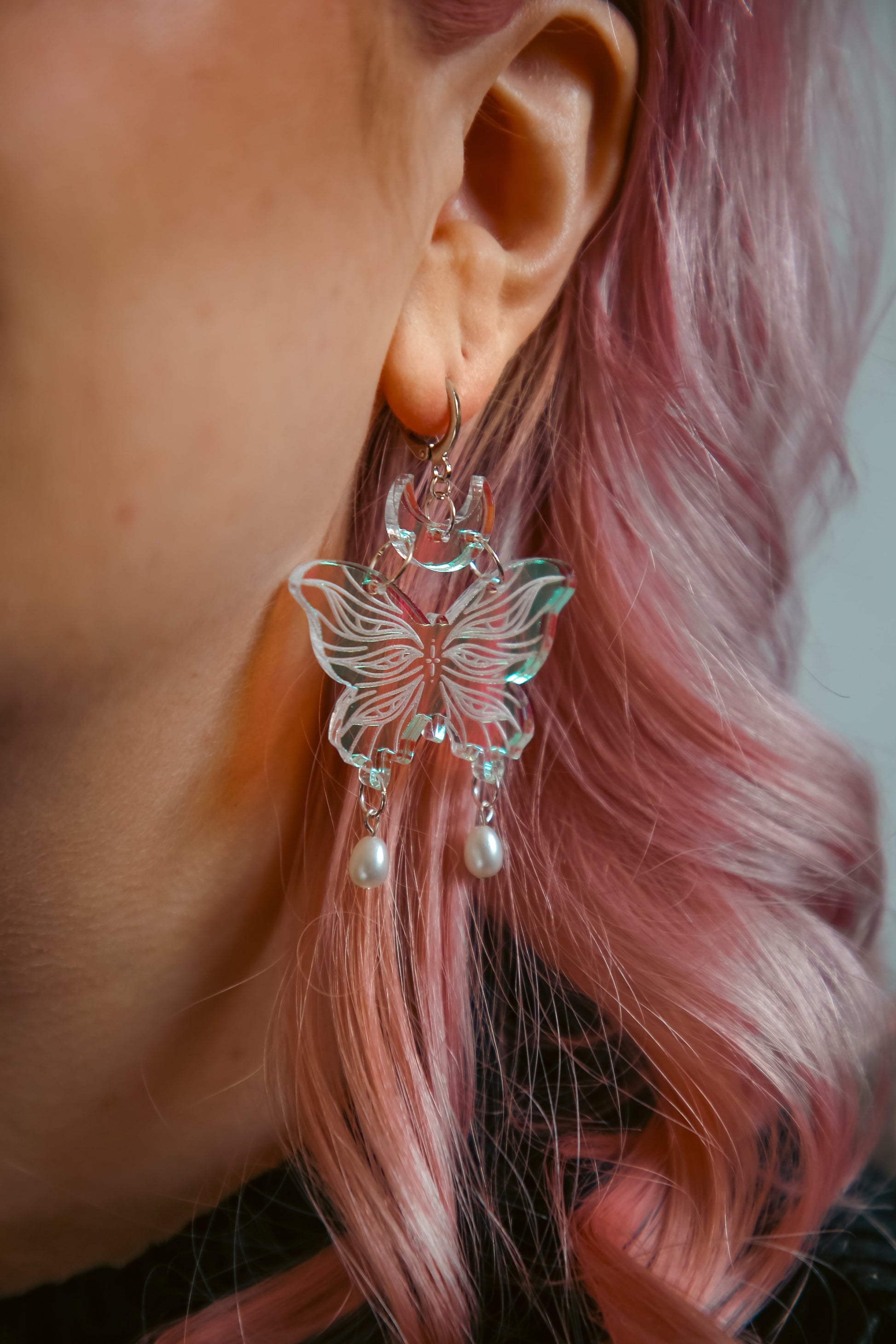small iridescent butterfly acrylic earring with pearls on a persons ear with pink hair