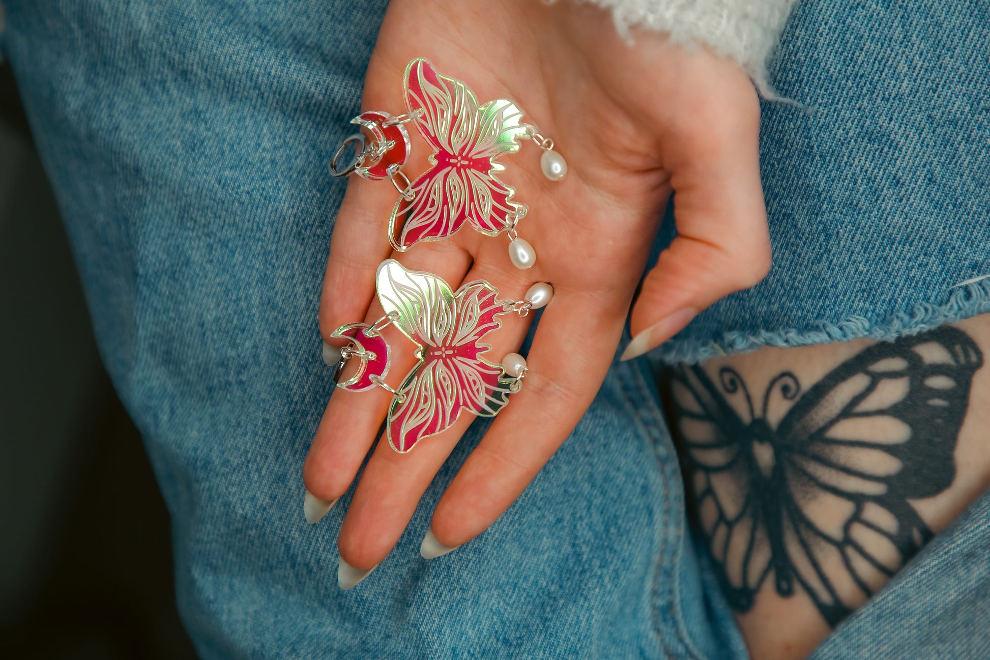 small iridescent butterfly acrylic earring with pearls against jeans and a butterfly tattoo