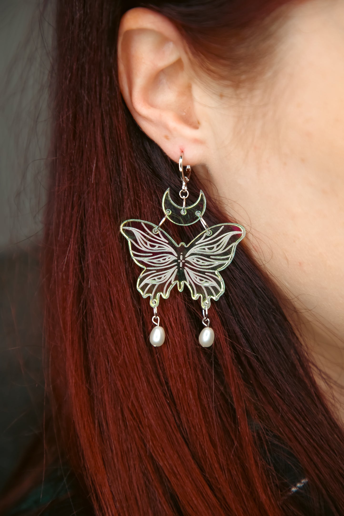 small iridescent butterfly acrylic earring with pearls on a persons ear with brown hair