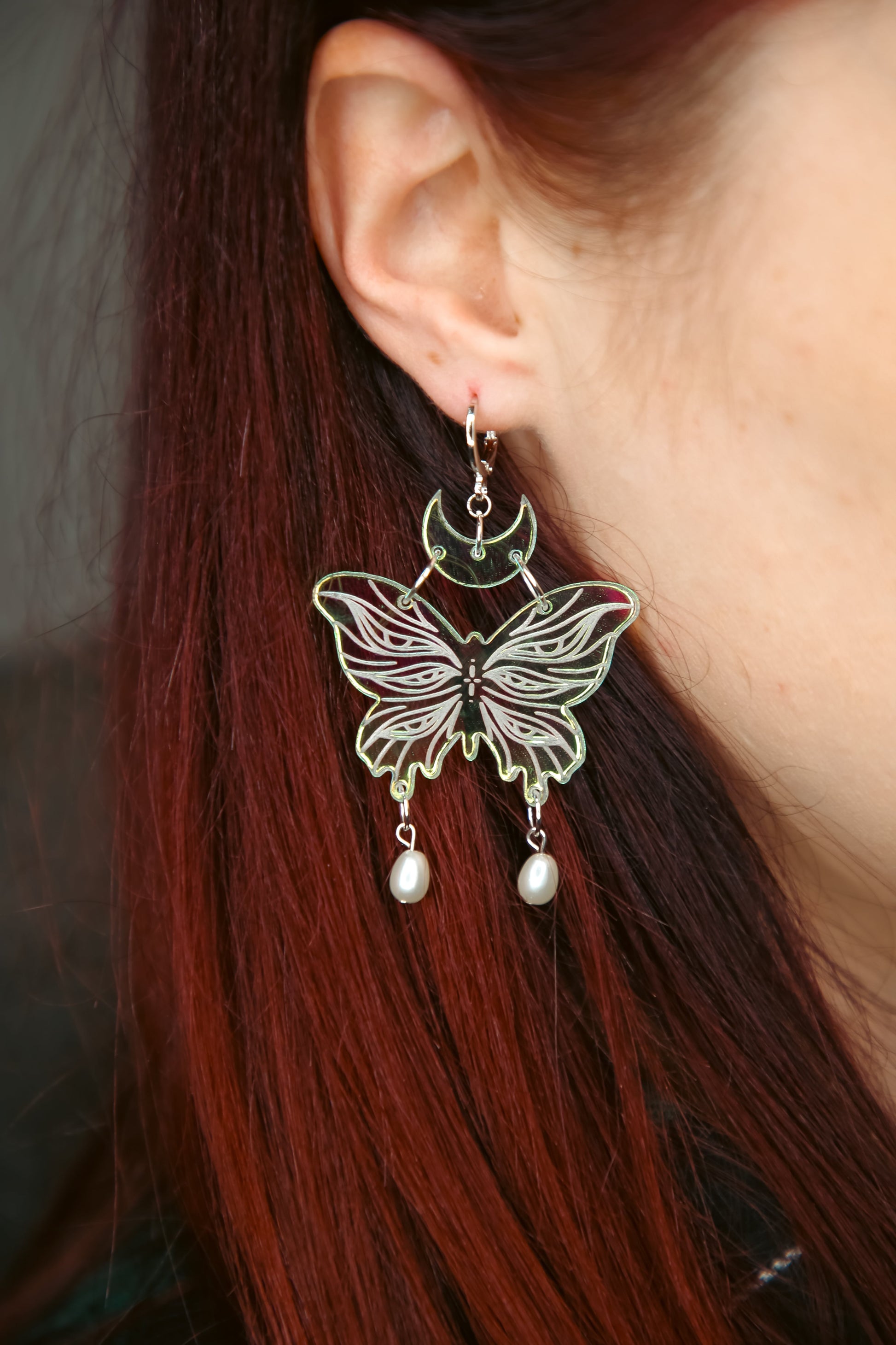 small iridescent butterfly acrylic earring with pearls on a persons ear with brown hair
