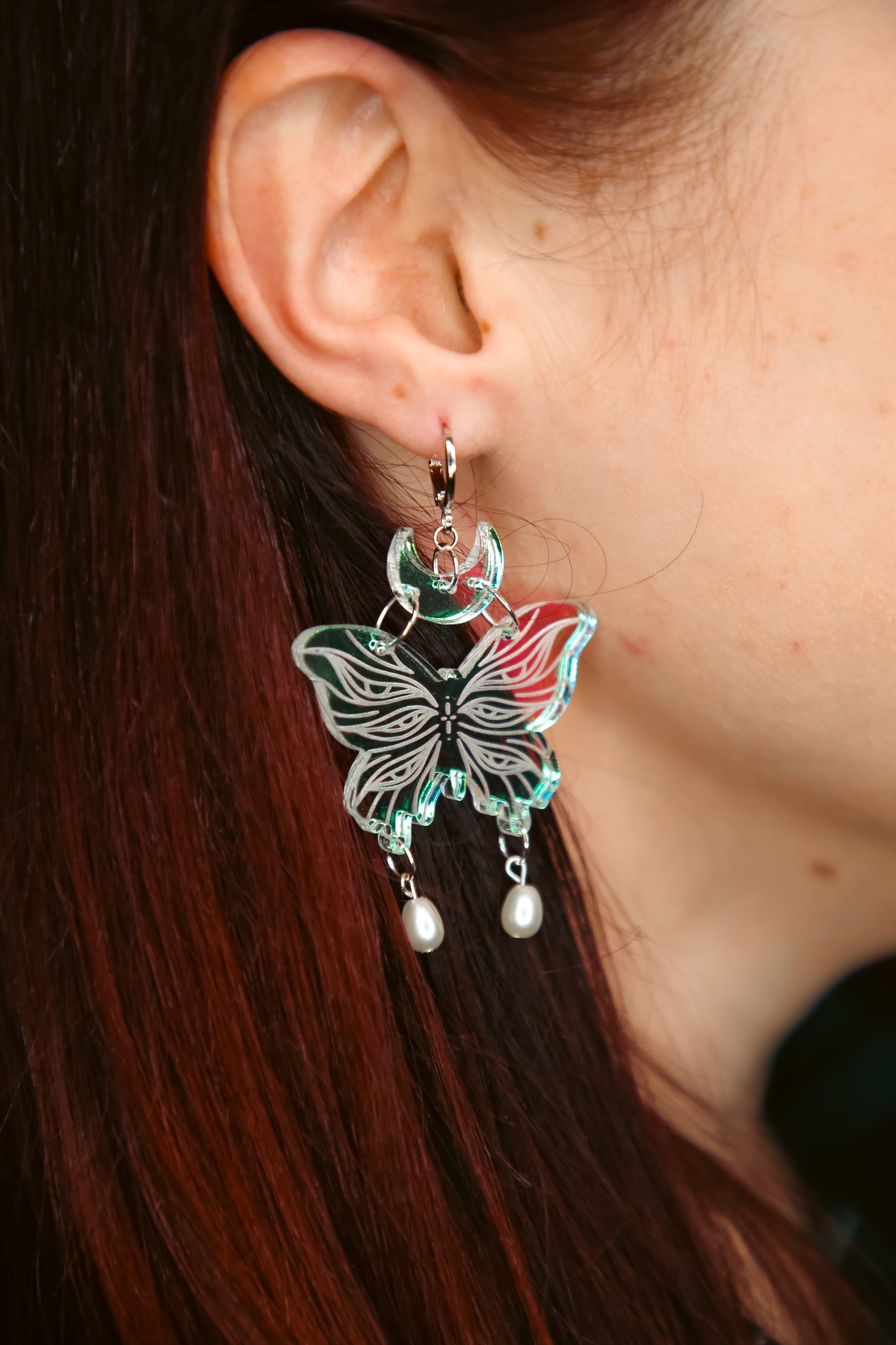 small iridescent butterfly acrylic earring with pearls on a persons ear with brown hair