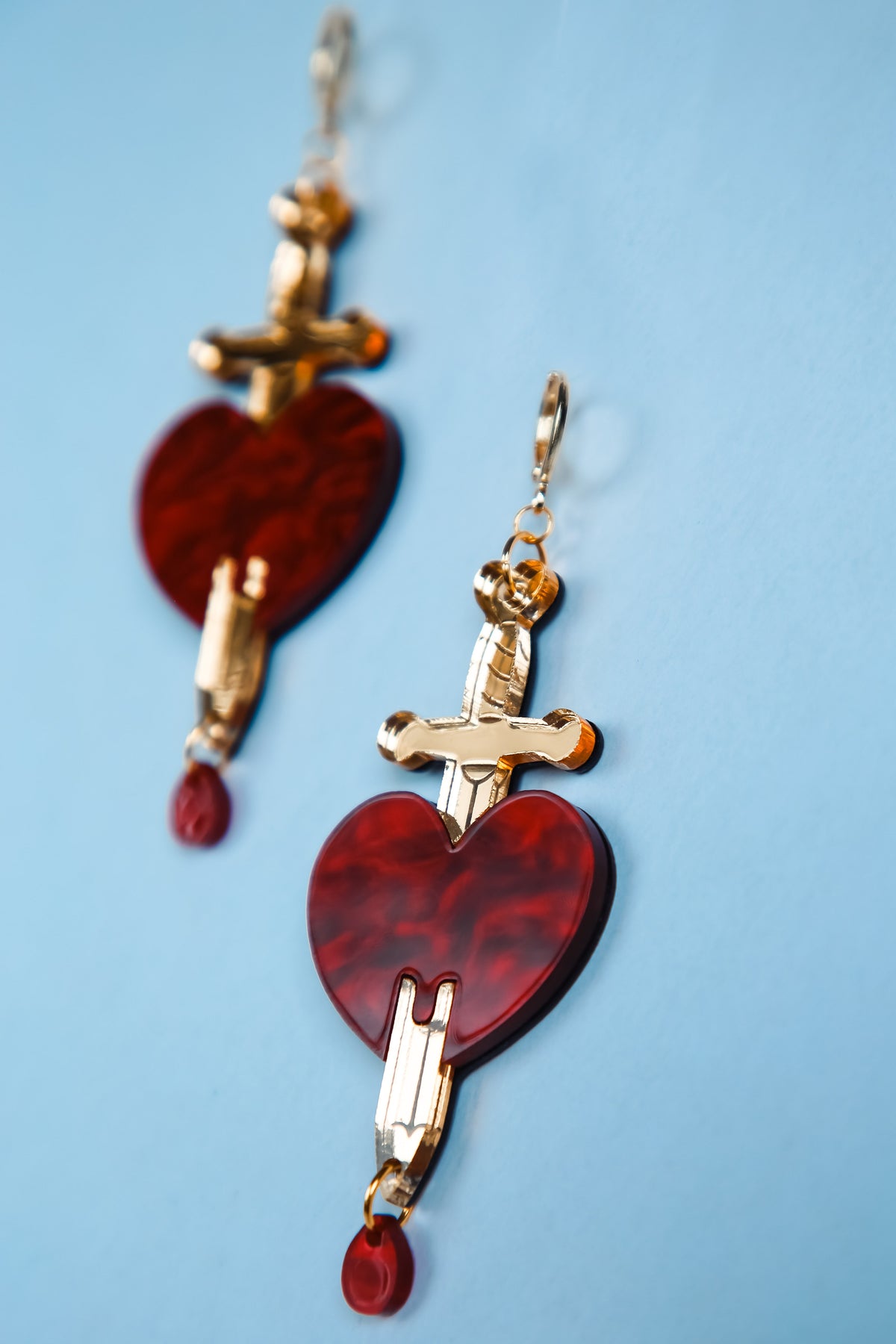 a pair of red and gold sword and heart acrylic earring with a blue background