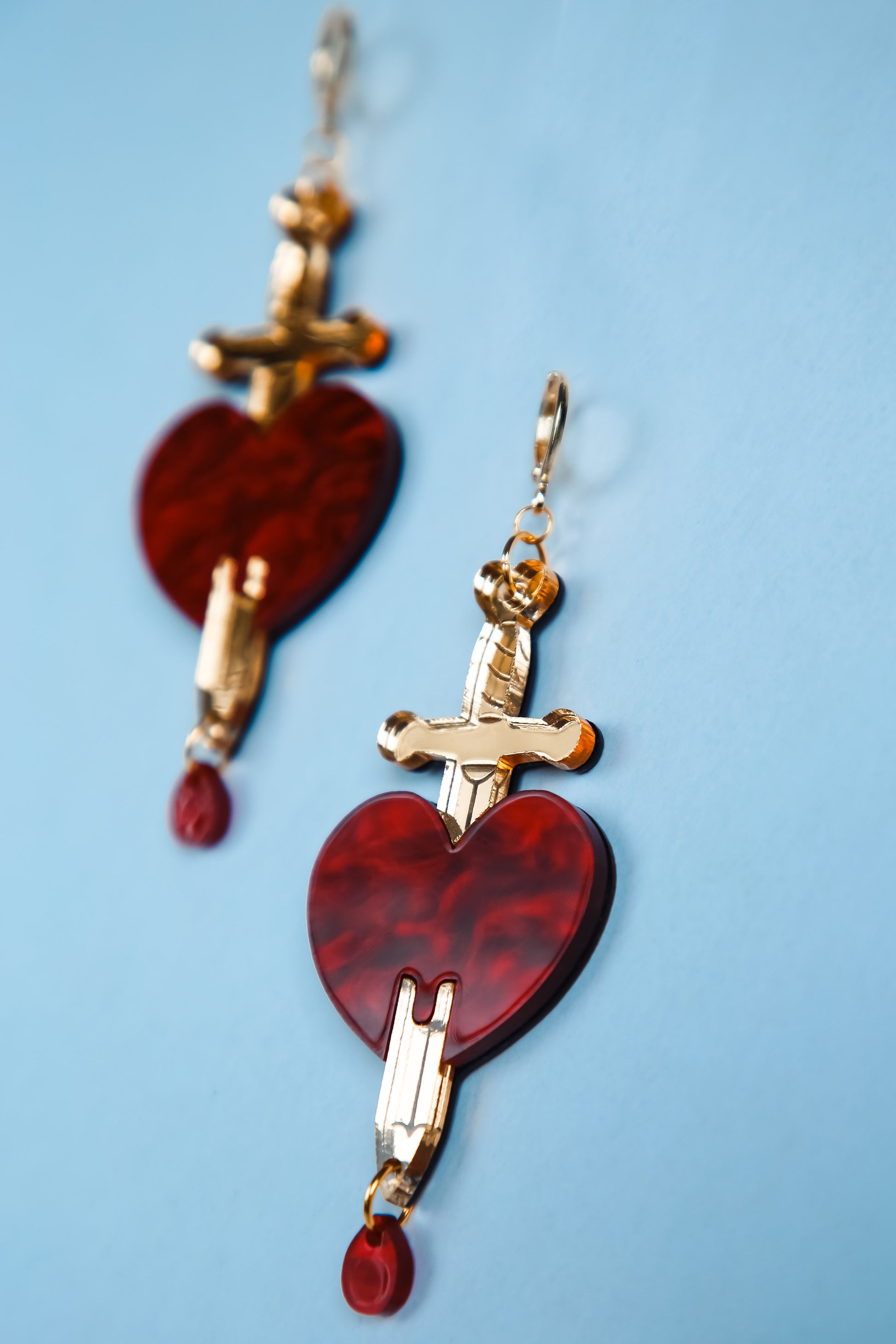 a pair of red and gold sword and heart acrylic earring with a blue background