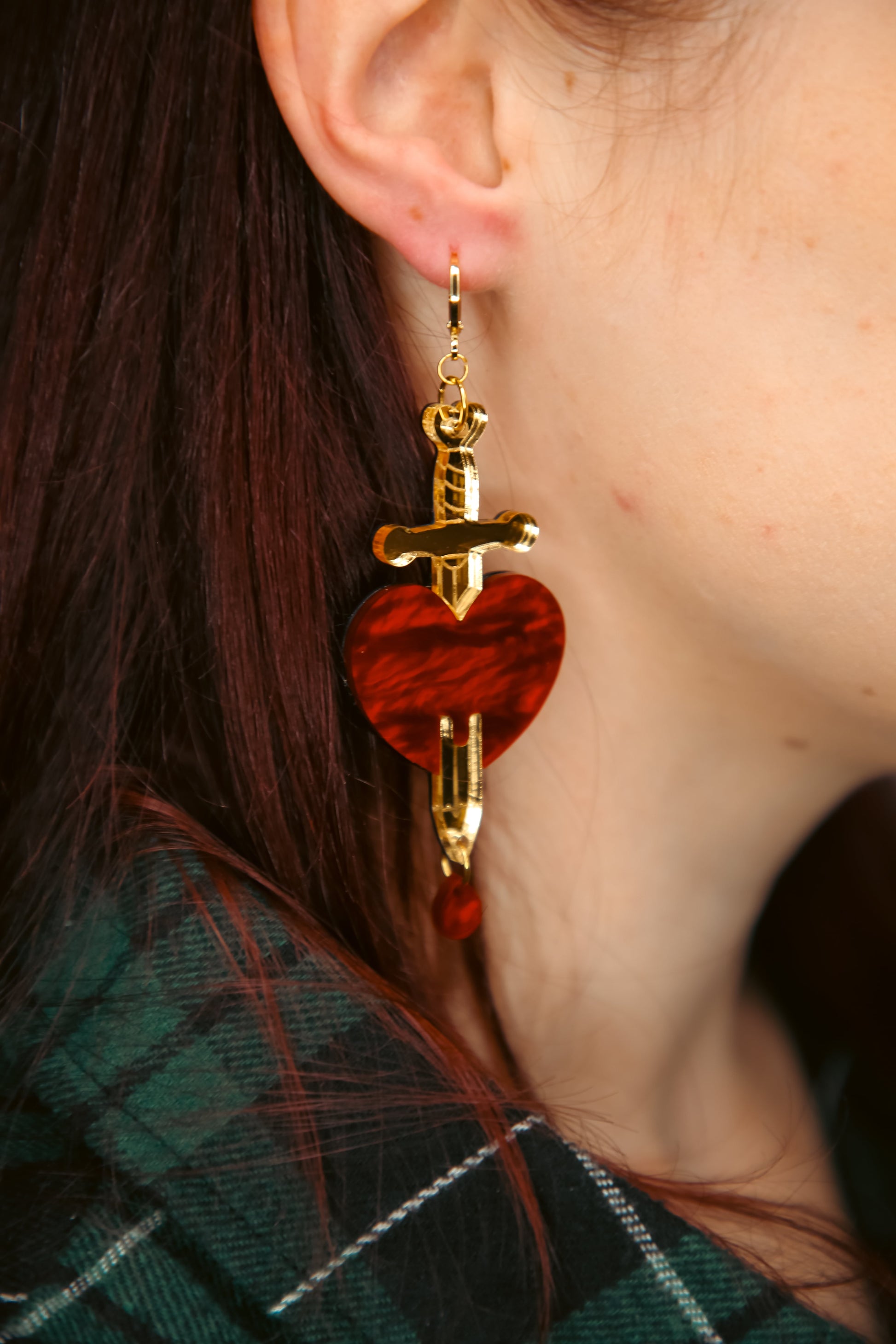 red and gold sword and heart acrylic earring being worn by a person with brown hair