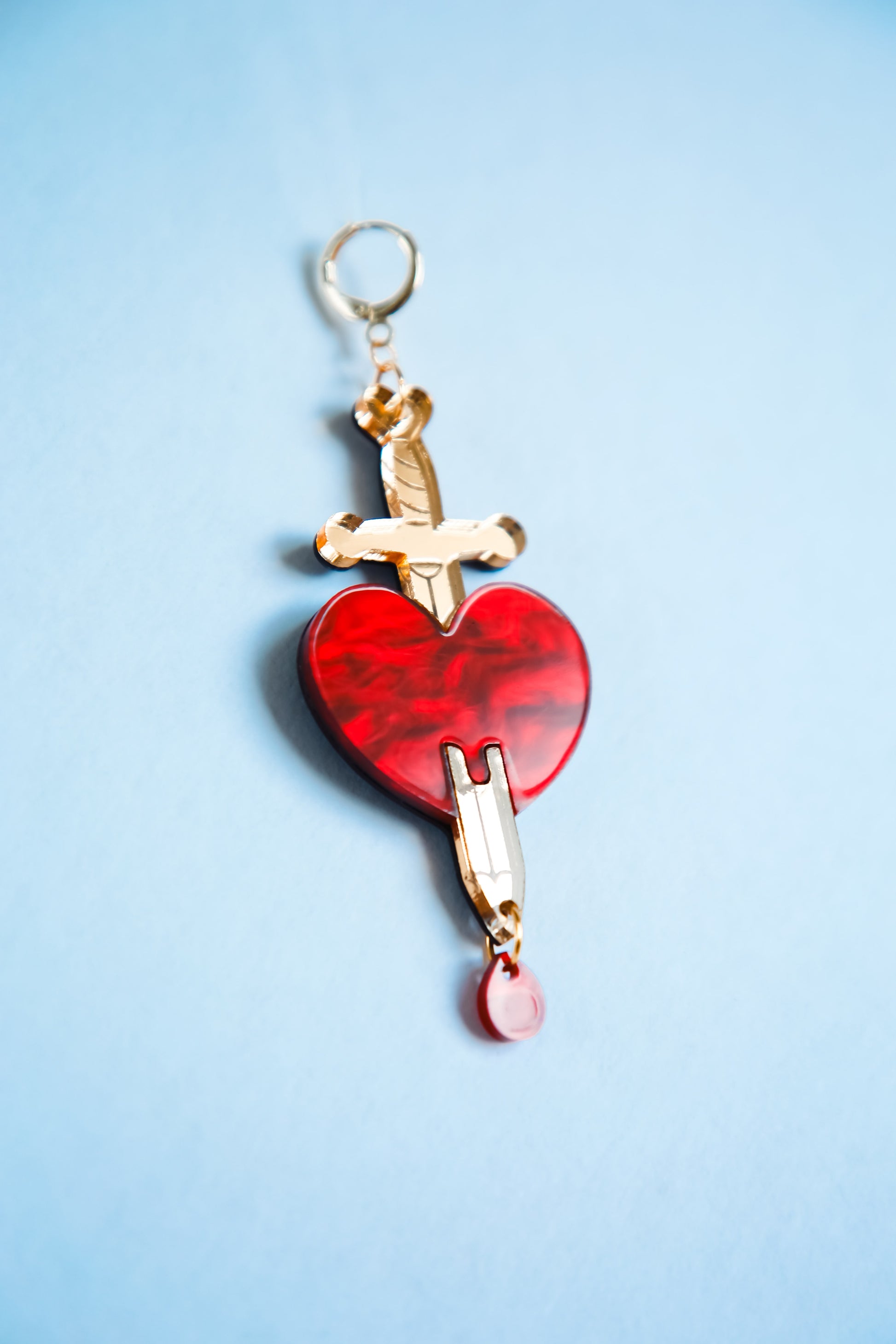 red and gold sword and heart acrylic earring on a blue background