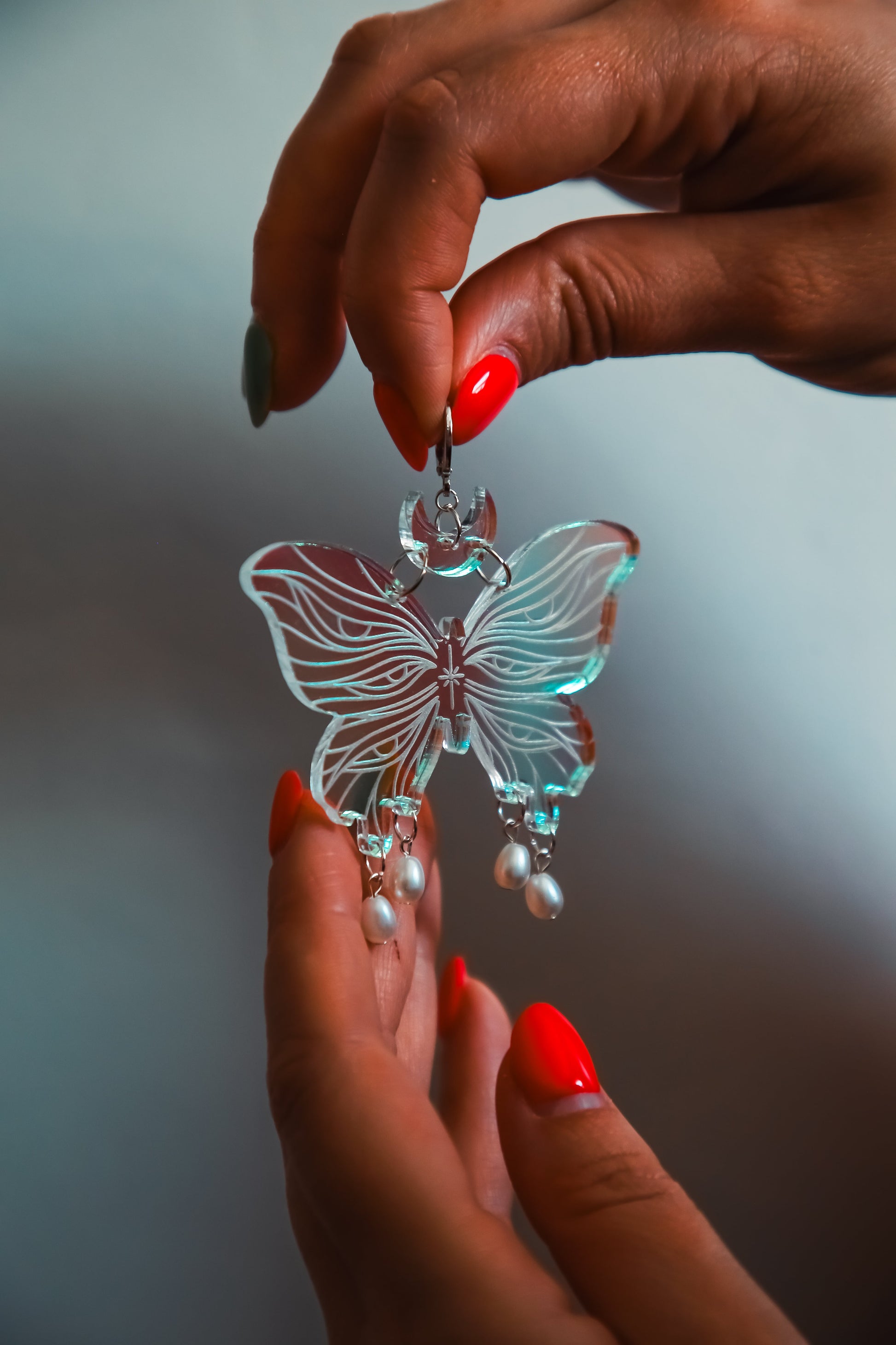 one large butterfly iridescent acrylic earrings with pearls held by hands