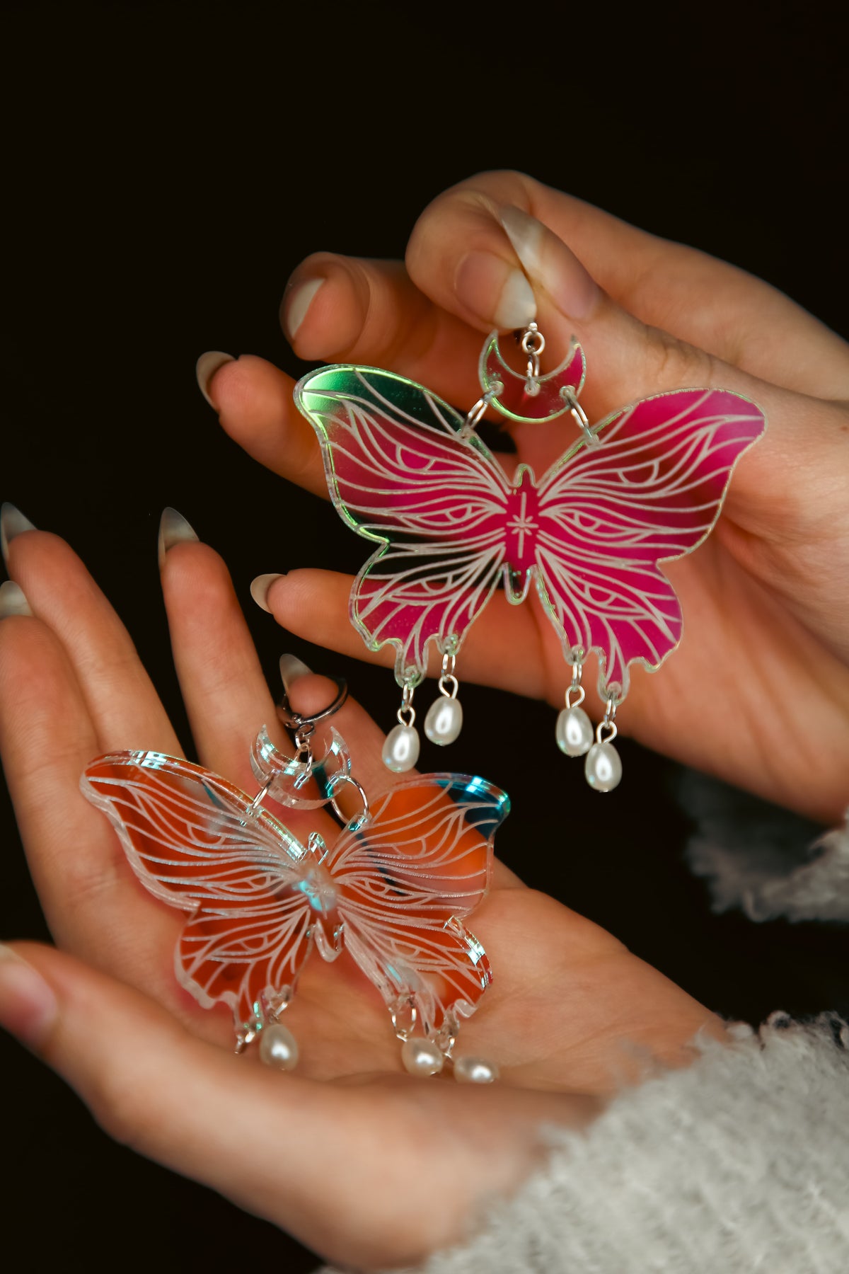 Two large butterfly iridescent acrylic earrings with pearls held by hands