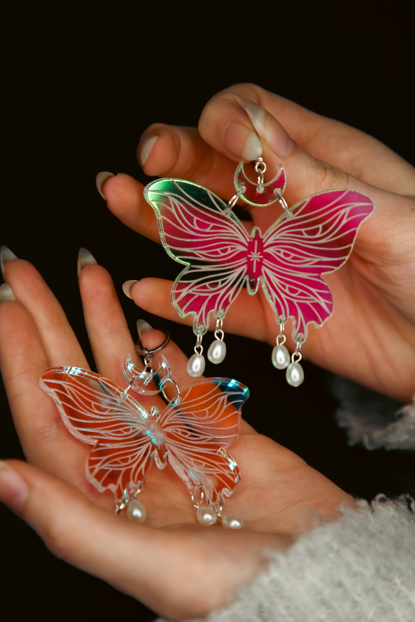 Two large butterfly iridescent acrylic earrings with pearls held by hands