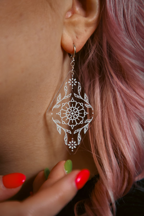 flower inspired acrylic earring made from transparent acrylic with a white design against pink hair