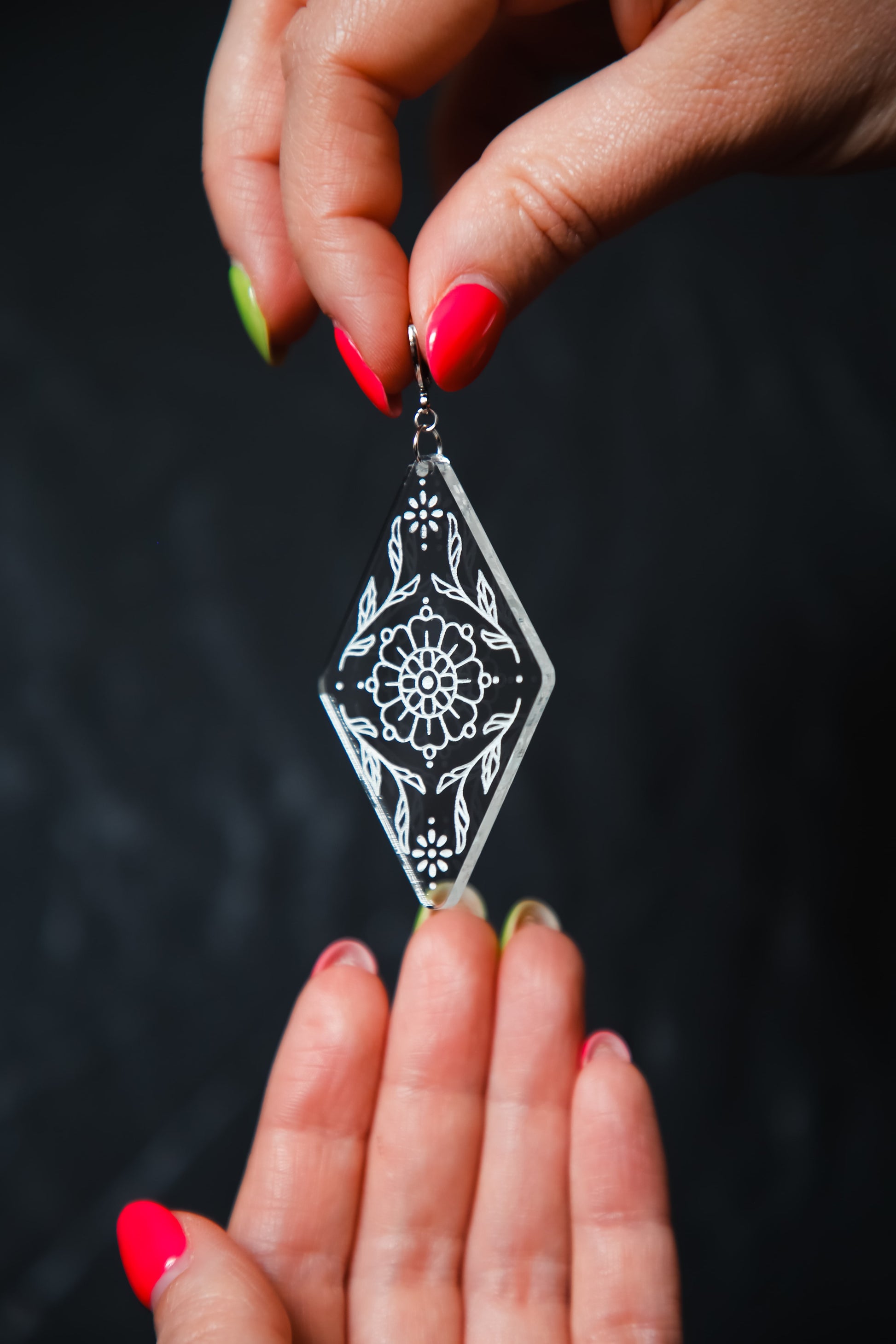 flower inspired acrylic earring made from transparent acrylic with a white design being held by hands