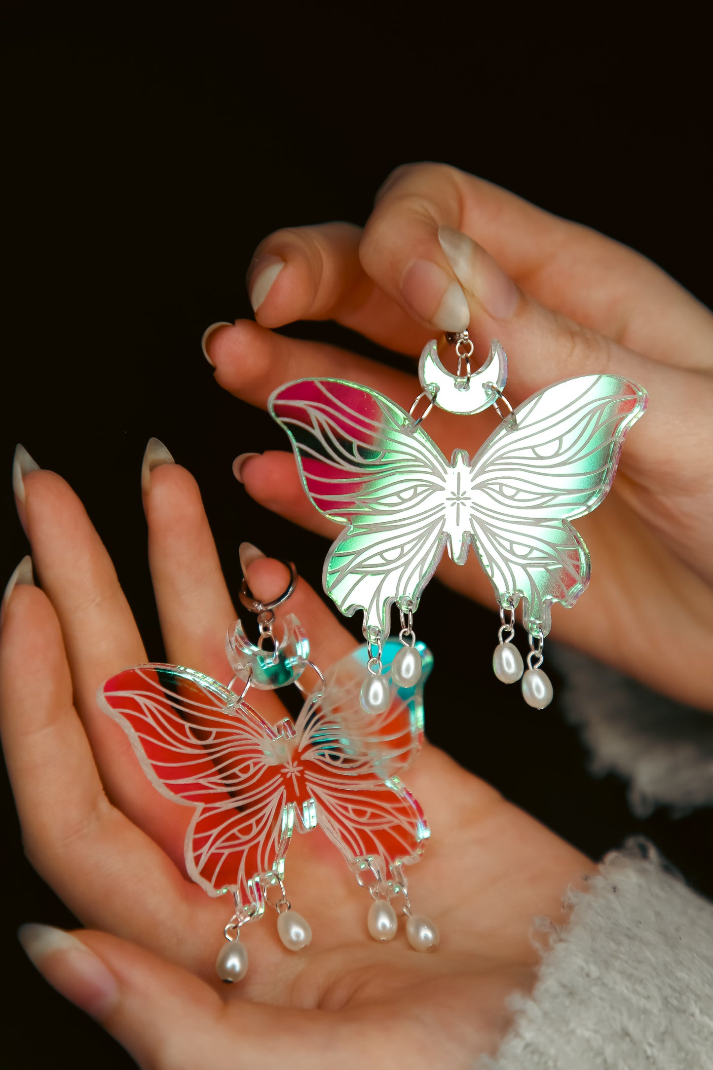 Two large butterfly iridescent acrylic earrings with pearls held by hands