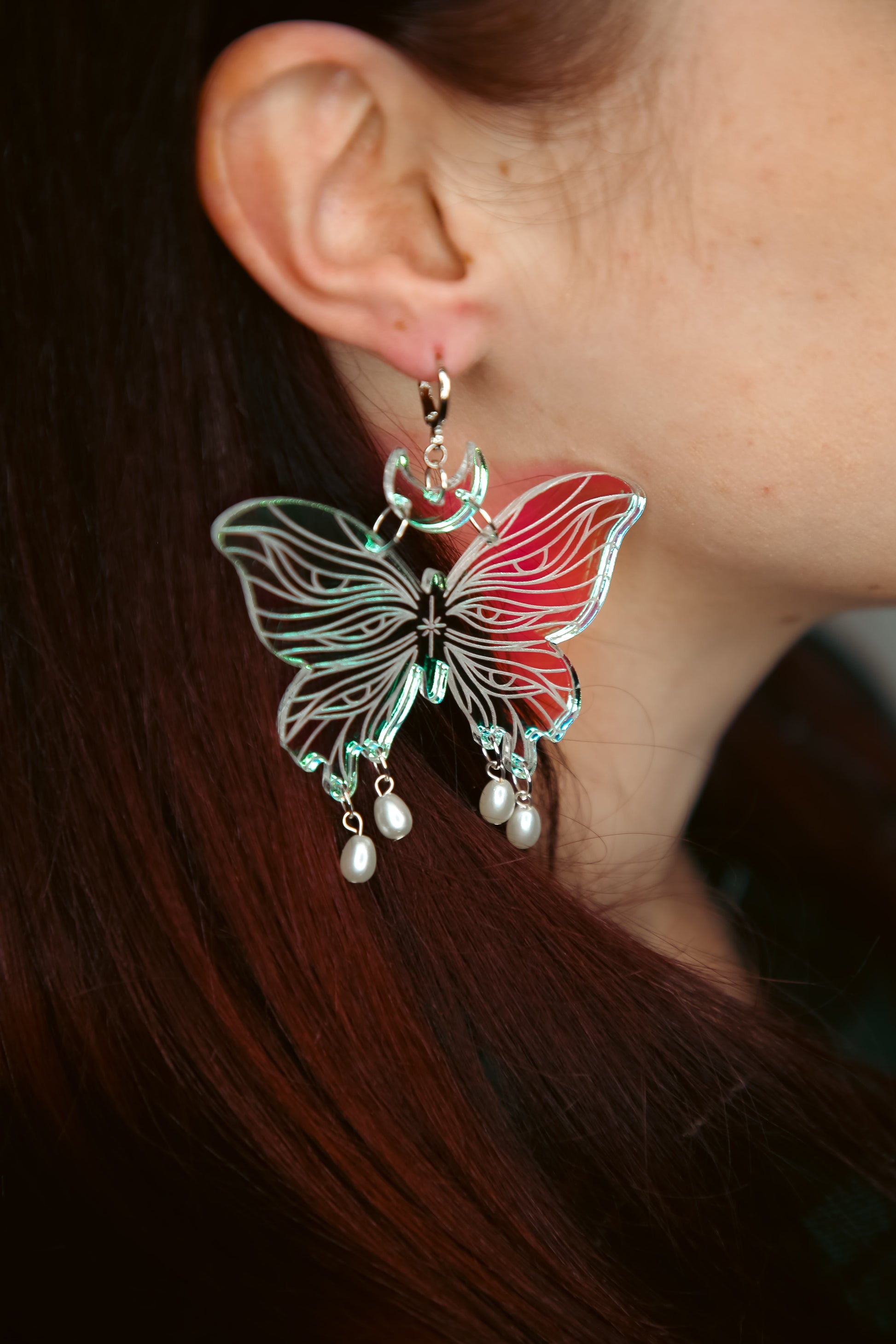 Large butterfly iridescent acrylic earrings with pearls worn with brown hair